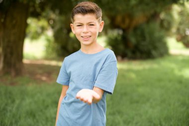 Güzel, beyaz, mavi tişörtlü çocuk dışarıda dikiliyor, gülümsüyor, avuç içi kadar yardım ve kabul görüyor..