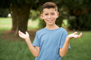 Neşeli, iyimser, güzel, beyaz, mavi tişörtlü çocuk elinde iki avuç içi fotokopi aletiyle dışarıda dikiliyor.