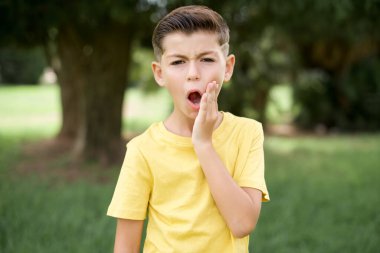 Açık havada duran sarı tişörtlü güzel beyaz çocuk çok şaşırmış görünüyor. Beklenmedik haberler, yüz ifadeleri konseptiyle şaşkına dönmüş..