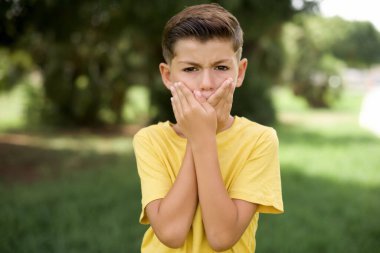 Sersemlemiş, beyaz, sarı tişörtlü bir çocuk. İki eli ağızda, hayret verici bir şeyden korkuyor.