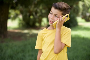 Hoş görünümlü, güzel, beyaz, sarı tişörtlü çocuk dışarıda dikiliyor. Güzel telefon görüşmeleri yapıyor ve yan yana bakıyor. Cep telefonuyla konuşurken güzel bir havası var ve gülümsüyor.