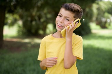Komik, güzel, beyaz, sarı tişörtlü çocuk dışarıda durup gülüyor, telefonla konuşuyor, eğleniyor, gözlerini kapıyor..