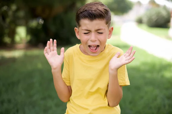 屋外に立って黄色のTシャツを着てクレイジー激怒した美しい白人の小さな子供の男の子は大声で叫び ジェスチャーを怒って怒りながら大声で叫ぶ 否定的な人間の感情の概念 — ストック写真