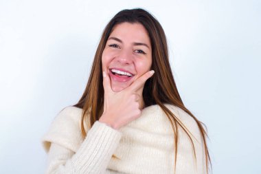 Beyaz süveter giyen genç bir kadın kameraya kendinden emin bir şekilde bakıyor kolları çapraz ve çenesi havada gülümsüyor. Olumlu düşünüyorum..