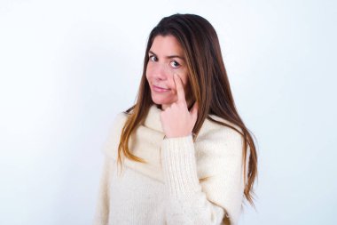 Beyaz süveter giyen genç bir kadın. Gözünü dikip jestini izliyor. Şüpheli bir ifade..