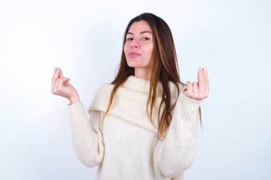 Beyaz süveter giyen, beyaz arka plan giyen, elleriyle para hareketi yapan, maaş ödemesi isteyen, milyonerlik işi yapan genç bir kadın.
