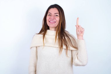 Beyaz süveter giyen genç bir kadın bir numarayı gösterip işaret ederken kendinden emin ve mutlu bir şekilde gülümsüyor..
