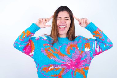Photo of crazy Young caucasian woman wearing vintage colorful sweater over white background screaming and pointing with fingers at hair closed eyes