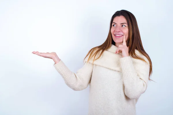白いセーターの白い背景を着た面白い若い女性がオープンパーム新製品を保持しています 買いたいんだけど — ストック写真