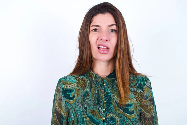 Portrait of dissatisfied young caucasian woman wearing floral dress over white background smirks face, purses lips and looks with annoyance at camera, discontent hearing something unpleasant