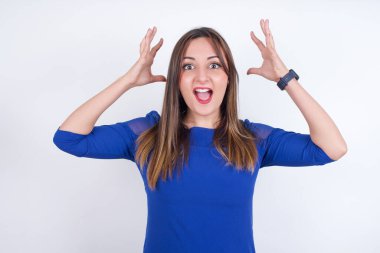 Beyaz arka plan üzerine mavi elbise giyen genç Arap kadın kameraya heyecanla bakıyor, ellerini başının üstüne kaldırıyor beklenmedik bir şey fark ediyor, ani haberlere tepki veriyor..