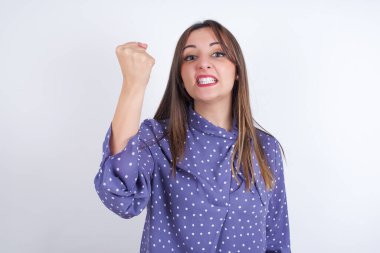 Vahşi genç Arap kadın, beyaz sırt çantasının üzerine benekli giysiler giyip yumruğunu sanki dövüşmeye ya da meydan okumaya hazırmış gibi tutuyor, bağırıyor ve yüzünde agresif bir ifade var..