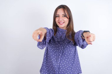 Beyaz arka plan üzerinde benekli giysiler giyen genç Arap kadının yakın plan portresi iki parmağıyla kameraya işaret ederek: 