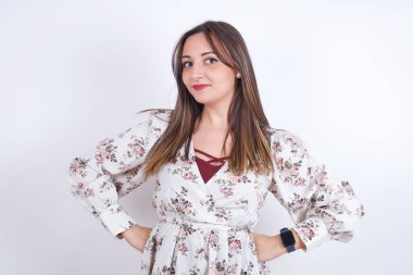 Beyaz sırt üstü çiçekli tişört giyen, belinde el ele tutuşan ve garip durumlara bakan komik sinirli Arap kadın..