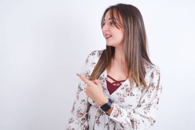 Mutlu gülümseyen genç Arap kadın, beyaz sırt üstü çiçekli gömlek giyip eliyle işaret ediyor. Alan ve reklam konseptini kopyala.