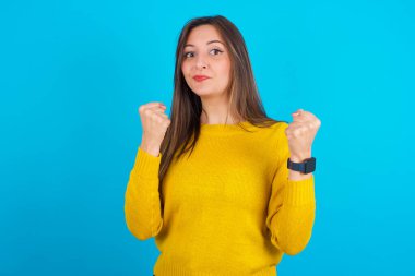 Mavi sırt çantasının üzerine sarı örülü süveter giyen sinirli genç Arap kadın öfkeyle yanaklarına vuruyor ve yumruklarını kaldırıyor öfke ve agresif duyguları ifade ediyor. Öfkeli model