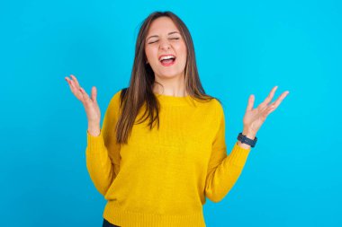 Sarı örgü süveter giyen çılgın öfkeli Arap kadın mavi arka bahçeye bağırıyor ve öfkeyle el kol hareketi yapıyor. Olumsuz insani duygular kavramı