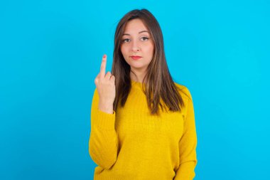 Mavi sırt çantasının üzerine sarı örülü süveter giyen genç Arap kadın orta parmak kötü işaretinin rahatsız etmemesini söylüyor. Kışkırtma ve kaba tavır.