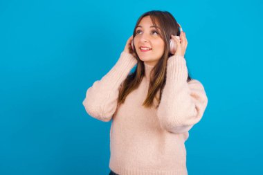 Mavi arka camının üzerine örülmüş süveter giyen genç Arap kadın stereo kulaklık takıyor ve müzik dinliyor. İnsanlar yaşam tarzı kavramını hobiliyor.