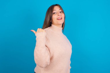 Etkileyici genç Arap kadın, örgü süveter giyip boş bir alanda mavi arka kapak noktası örüyor.