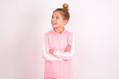 Dreamy rest relaxed little caucasian kid girl wearing sport clothing over white background crossing arms, looks good copyspace