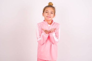 little caucasian kid girl wearing sport clothing over white background holding something with open palms, offering to the camera.