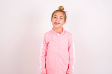 little caucasian kid girl wearing sport clothing over white background showing grimace face crossing eyes and showing tongue. Being funny and crazy