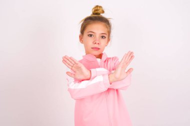 little caucasian kid girl wearing sport clothing over white background has rejection expression crossing arms and palms doing negative sign, angry face.