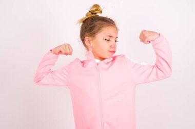 little caucasian kid girl wearing sport clothing over white background showing arms muscles smiling proud. Fitness concept.