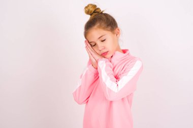 little caucasian kid girl wearing sport clothing over white background sleeping tired dreaming and posing with hands together while smiling with closed eyes.
