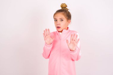 little caucasian kid girl wearing sport clothing over white background Moving away hands palms showing refusal and denial with afraid and disgusting expression. Stop and forbidden.