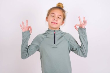 little caucasian kid girl wearing sport clothing over white background relax and smiling with eyes closed doing meditation gesture with fingers. Yoga concept.