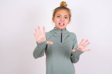 little caucasian kid girl wearing sport clothing over white background afraid and terrified with fear expression stop gesture with hands, shouting in shock. Panic concept.