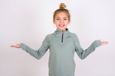 Cheerful cheery optimistic little caucasian kid girl wearing sport clothing over white background holding two palms copy space