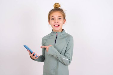 little caucasian kid girl wearing sport clothing over white background holding in hands showing new cell,