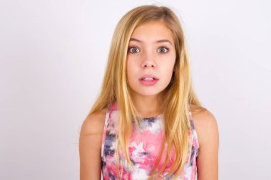 Stunned little caucasian kid girl wearing sport clothing over white background  stares reacts on shocking news. Astonished MODEL holds breath