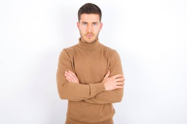 Serious pensive young caucasian man wearing turtleneck over white background feel like cool confident entrepreneur cross hands.