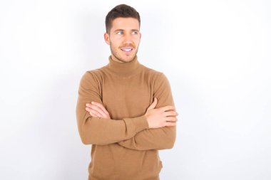 Dreamy rest relaxed young caucasian man wearing turtleneck over white background crossing arms, looks good copyspace