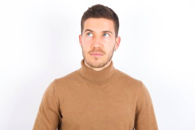young caucasian man wearing turtleneck over white background looking aside into empty space thoughtful
