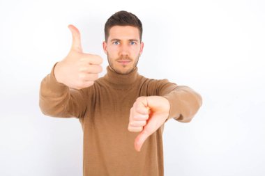 young caucasian man wearing turtleneck over white background showing thumbs up and thumbs down, difficult choose concept