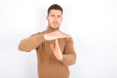 young caucasian man wearing turtleneck over white background being upset showing a timeout gesture, needs stop, asks time for rest after hard work, demonstrates break hand sign