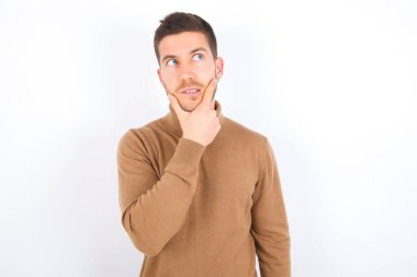 young caucasian man wearing turtleneck over white background Thinking worried about a question, concerned and nervous with hand on chin.