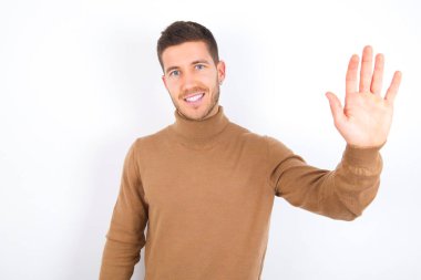 young caucasian man wearing turtleneck over white background Waiving saying hello happy and smiling, friendly welcome gesture.