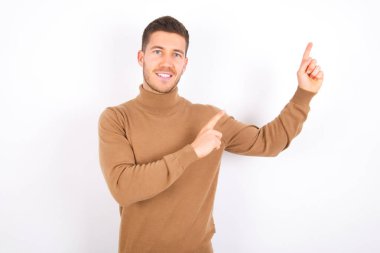 young caucasian man wearing turtleneck over white background indicating finger empty space showing best low prices, looking at the camera
