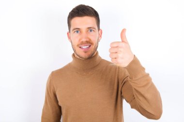 young caucasian man wearing turtleneck over white background doing happy thumbs up gesture with hand. Approving expression looking at the camera showing success.