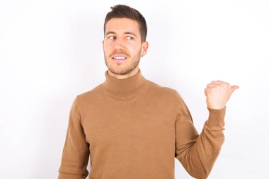 Charming young caucasian man wearing turtleneck over white background looking at copy space having advertisements