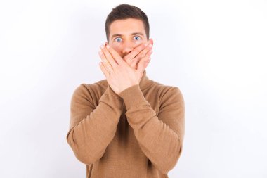 young caucasian man wearing turtleneck over white background shocked covering mouth with hands for mistake. Secret concept.