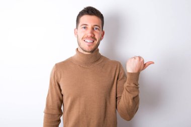Lovely young caucasian man wearing turtleneck over white background pointing aside with forefinger, showing at copy space having news about bargains