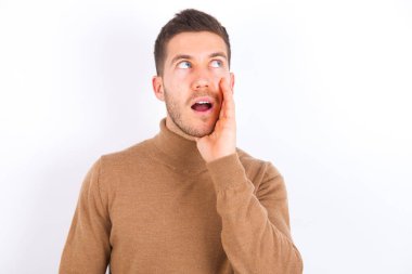 young caucasian man wearing turtleneck over white background hear incredible private news impressed scream share