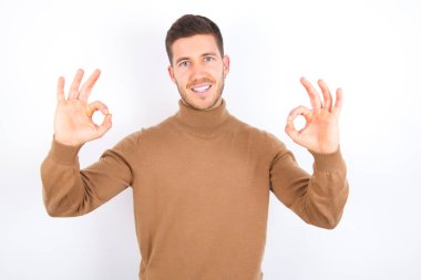 young caucasian man wearing turtleneck over white background showing both hands with fingers in OK sign. Approval or recommending concept